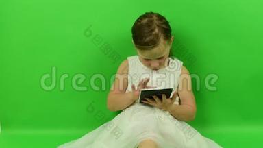 可爱的小女孩在色度键背景上阅读电子书。 穿着浪漫裙子的小女孩。 白色婚纱礼服