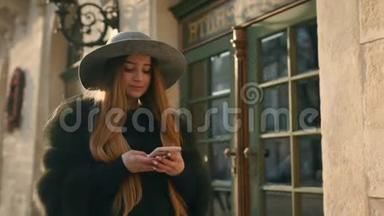 美丽的黑发女人戴着灰色帽子站在<strong>拥挤</strong>的城市<strong>街道</strong>上，用她的手机发短信