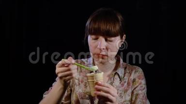 年轻的女人正在用勺子在黑色的背景上吃冰淇淋。