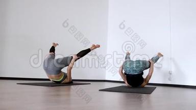 两个女孩在健身房里做一个运动。 彼拉多哈塞尔。 勒兹纳亚在她的背上，她的腿抬起，使她成为