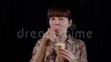 年轻的女人正在<strong>用勺子</strong>在黑色的背景上吃冰淇淋。