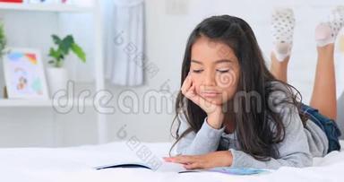 美丽的亚洲年轻的黑发女人在家里的床上看书，微笑着面对