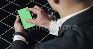 年轻的商人使用带有绿色屏幕触摸板的smarthpone，并在咖啡馆打手势接近。 一个拿着手机的家伙，敲