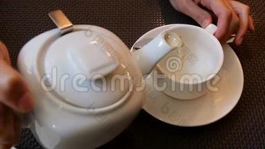 女孩用白色的小杯子从一个小白瓷茶壶里倒茶