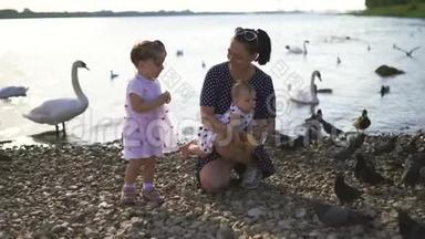 年轻的母亲带着她的小女儿在河边喂天鹅和<strong>小鸭</strong>子，小鸟在河边吃面包，穿着点缀的裙子