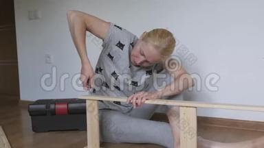 一个<strong>女人坐在地板上</strong>收集房间里<strong>的</strong>木制家具，用螺丝刀拧螺丝。