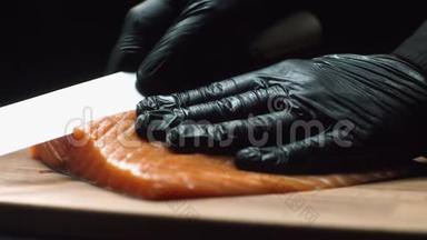 配红色三文鱼的特写厨师。 职业厨师戴着黑色手套，手里拿着一块新鲜的鲑鱼，准备