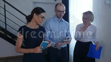 自信的人在上班的时候走在公司走廊上，一边用数字平板电脑阅读金融新闻信息