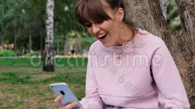 照片中年轻的白人美女微笑着穿着粉色运动衫在智能手机上聊天