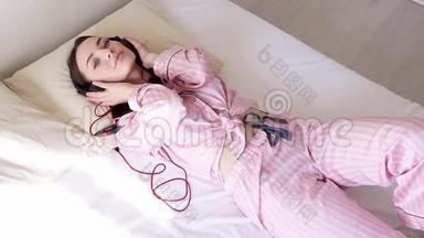 穿着睡衣的女人躺在床上，用耳机随着音乐跳舞