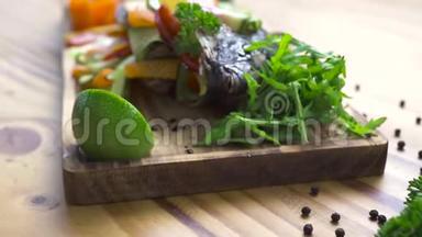 用新鲜蔬菜和香料在木板上烤鱼。 海鲜餐桌上烤鱼的食物组成