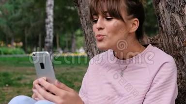照片中年轻的白人女孩微笑着穿着粉色运动衫，在智能手机上聊天