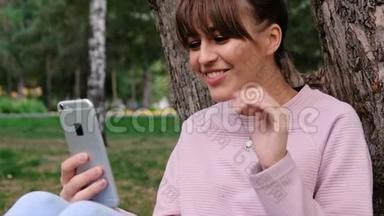 照片中年轻的白人女孩微笑着穿着粉色运动衫，在智能手机上聊天