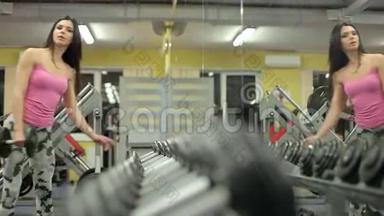 运动的女人从健身房里的一排哑铃里拿出一个哑铃。
