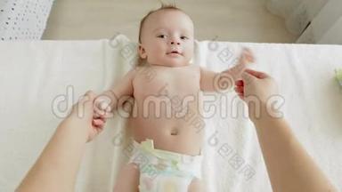 在卧室里躺在换洗的桌子上按摩3个月大的婴儿的年轻母亲的POV照片。 婴儿健康成长的概念