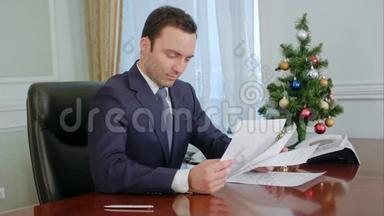 年轻商人在新年树附近的书桌旁阅读文件并签名