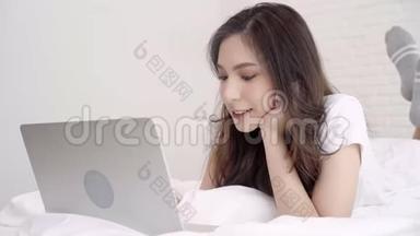 美丽的亚洲女人在卧室里躺在床上玩电脑或笔记本电脑。