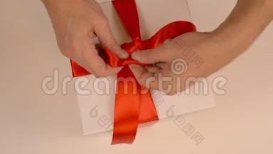 关闭顶部<strong>视图高角度</strong>。 男人的手从礼品盒上的缎带上伸直一个红色的蝴蝶结。 准备礼物