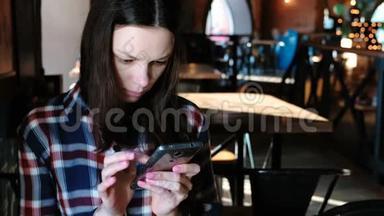 坐在咖啡馆里的女人在电话里发信息或使用互联网。 穿着格子衬衫。