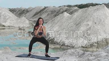穿着黑色运动服的运动型黑发女孩在一个白色粉笔采石场和蓝色的水对抗。蹲下