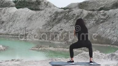 穿着黑色运动服的运动型黑发女孩在一个白色粉笔采石场和蓝色的水对抗。蹲下