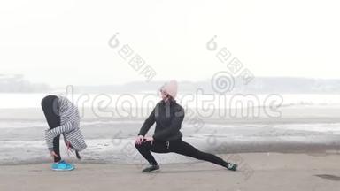 两个运动的女人站<strong>在</strong>海滩上热身。 天气寒冷