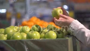 一个女孩在商店的<strong>蔬菜货架</strong>上挑选绿色的苹果。