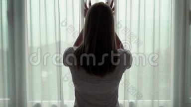 年轻女人揭开窗帘的剪影，<strong>望</strong>着<strong>窗外</strong>。 在外面欣赏海景。 慢动作100fps..