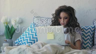 年轻的女人在卧室的笔记本电脑上写课文，上面盖着毯子。