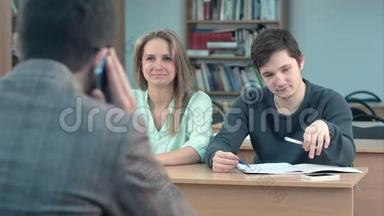 一群大学生坐在礼堂的<strong>课桌</strong>前等着老师，而他正在谈论