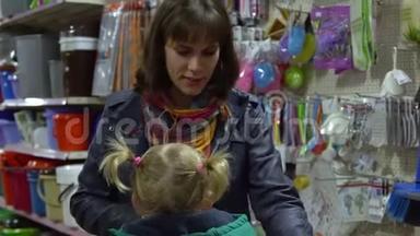 一个年轻的女人带着一个孩子在超市选择<strong>商品</strong>。 妈妈在手推车上驾驶一个小女孩。 考虑一下货物