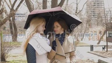 在公园里见朋友。 下雨时，两个金发女孩和一个黑发女孩站在伞下。 一个年轻人