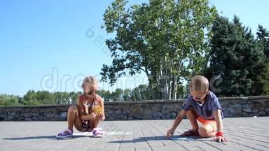 <strong>孩子</strong>们，一个男孩和一个女孩戴着太阳镜，用彩色蜡笔在沥青上<strong>画画</strong>，街道瓷砖。 炎炎夏日..