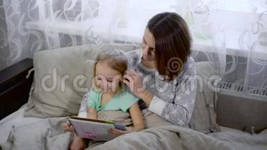 快乐的<strong>一家人</strong>在睡觉互相享受。 漂亮的年轻妈妈正在给她可爱的小<strong>女儿</strong>读一本书。 妇女