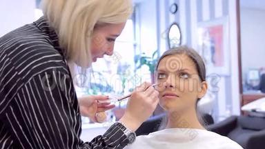 化妆师用刷子和海绵在年轻女子脸上涂抹粉底