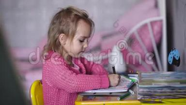 穿着粉红色开襟羊毛衫的漂亮小女孩正在幼儿园用彩色铅笔画插图。 小天才
