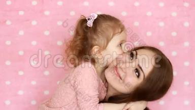 母女拥抱，微笑，玩得开心，笑着亲吻。 年轻女子和她的孩子在粉色上的特写肖像