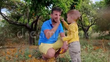 年轻的<strong>父亲和儿子在</strong>橙色的花园里拍掌。 爸爸<strong>和儿子</strong>五只手