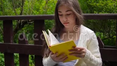 一幅严肃的少女阅读书和翻页的肖像，春天倚在森林的长凳上
