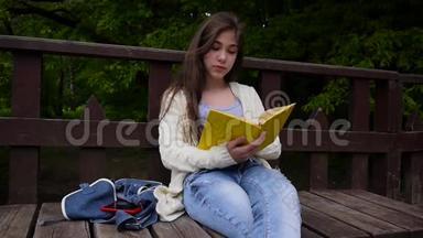 一幅严肃的少女阅读书和翻页的肖像，春天倚在森林的长凳上