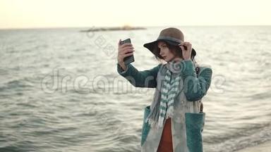 日落时在海滩上自拍的女孩。 一位身穿<strong>秋装</strong>的年轻漂亮女子在手机上拍照