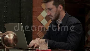 一个英俊的商人在<strong>高档</strong>酒吧喝酒的时候，在他的笔记本电脑上工作