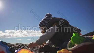 一个<strong>小孩</strong>子在海边玩玩具，穿着<strong>冬天</strong>的衣服和帽子。