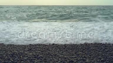 波浪冲刷卵石滩.. 波浪再次拍打着一片光滑的海滩，用白色的泡沫覆盖它。 波浪撞击