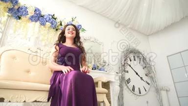 穿着晚礼服的年轻女子穿着紫色衣服坐在豪华的室内沙发上