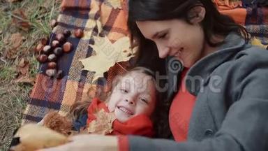 美丽<strong>的</strong>母亲和她可<strong>爱的</strong>小女儿躺在格子布上，在秋天公园玩<strong>枫叶</strong>