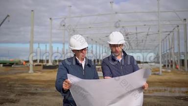 男工程师<strong>主管</strong>戴着安全帽，绘制蓝图并讨论计划。 他们检查质量