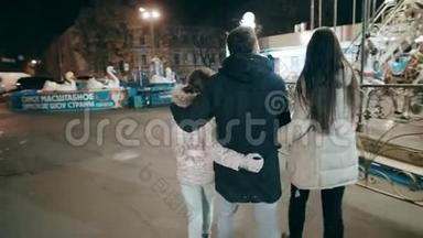 一个美丽的年轻家庭晚上在游乐园散步。 家庭度假在Lunapark。