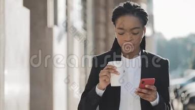 一位年轻的非洲裔美国女商人穿着西装，在城市里<strong>走来走</strong>去，喝着咖啡，用着