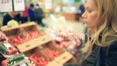 一个女人在蔬菜货架上的超市里买蔬菜和水果。 男人选择番茄